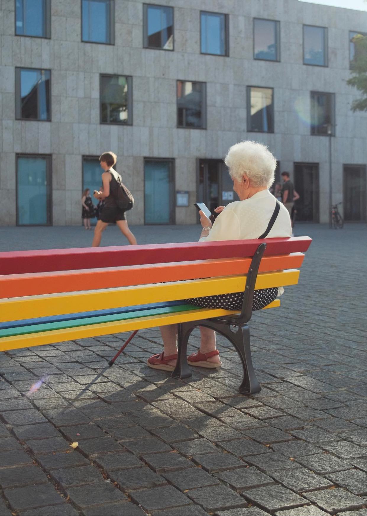 Old woman sitting on rainbow bench